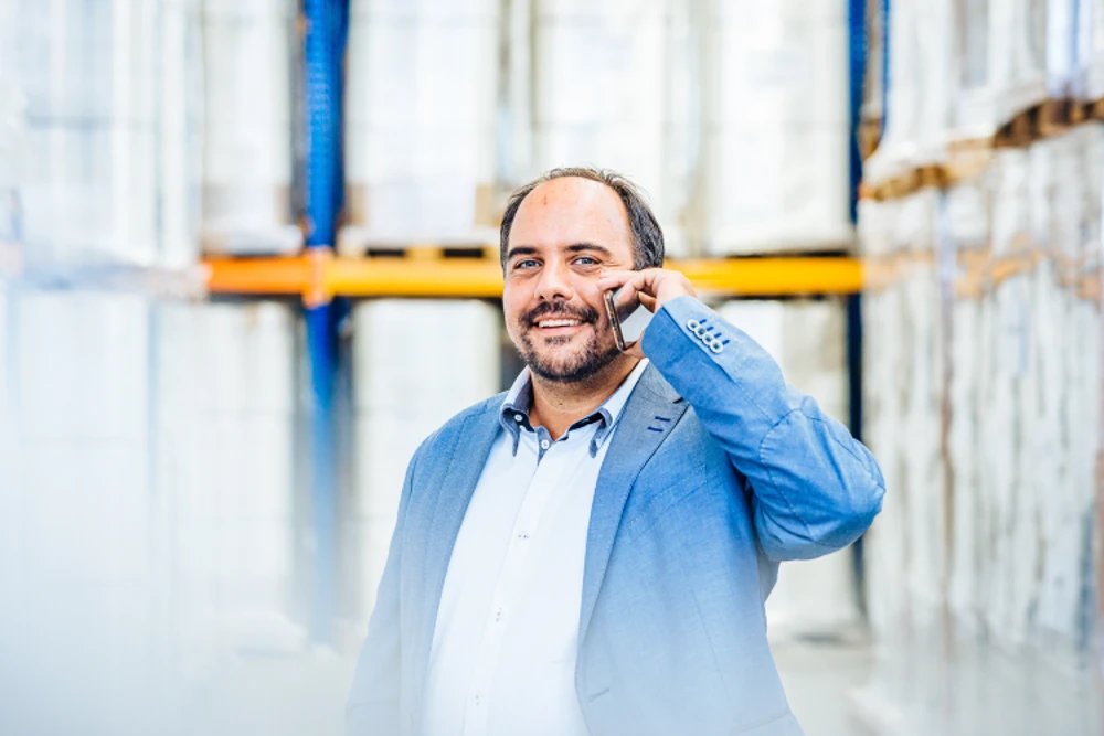 Experte für Palettenwickler Sascha Vogel lächelt, während er einen zufriedenen Kunden am Telefon zu einem neuen Palettenwickler berät.